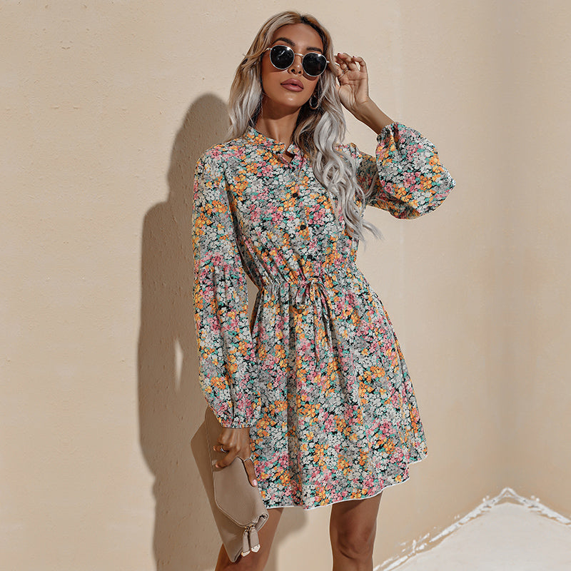 A woman poses confidently in a yellow floral print dress with bishop sleeves and a v-neck.