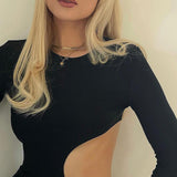 Close-up of a woman's upper body wearing a long-sleeved black dress with a side cut-out, featuring a delicate gold necklace.