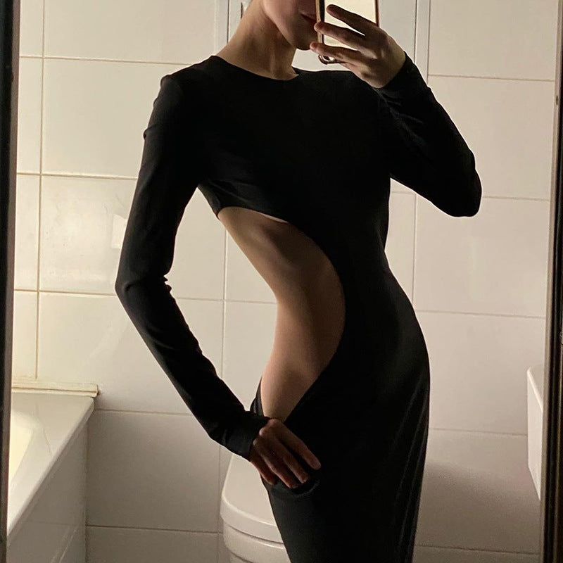 A woman in a black long-sleeved dress with a large cut-out on the side poses for a mirror selfie in a bathroom.