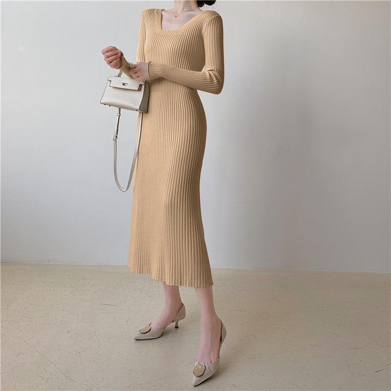 A woman wearing a beige ribbed knit midi dress with long sleeves and a square neckline, accessorized with a handbag and heels.
