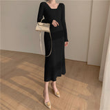 A woman wearing a black ribbed knit midi dress with long sleeves and a square neckline, paired with beige heels and a white handbag.