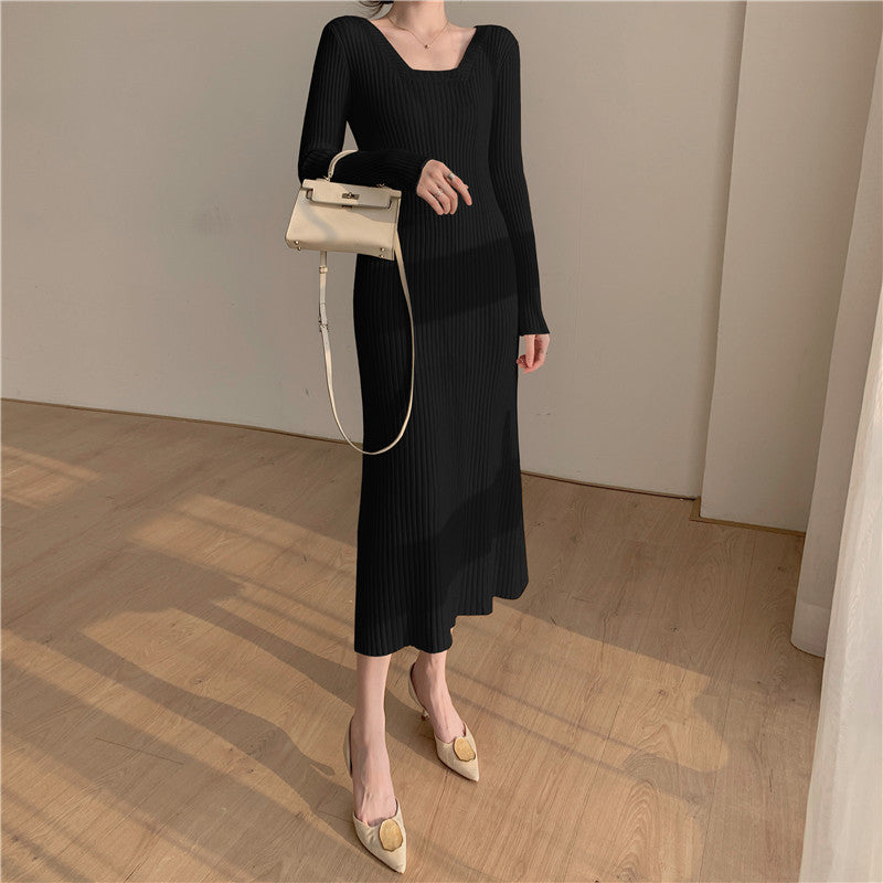 A woman wearing a black ribbed knit midi dress with long sleeves and a square neckline, paired with beige heels and a white handbag.