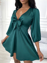 woman wearing a green satin mini dress with a tie-front detail and puffed sleeves