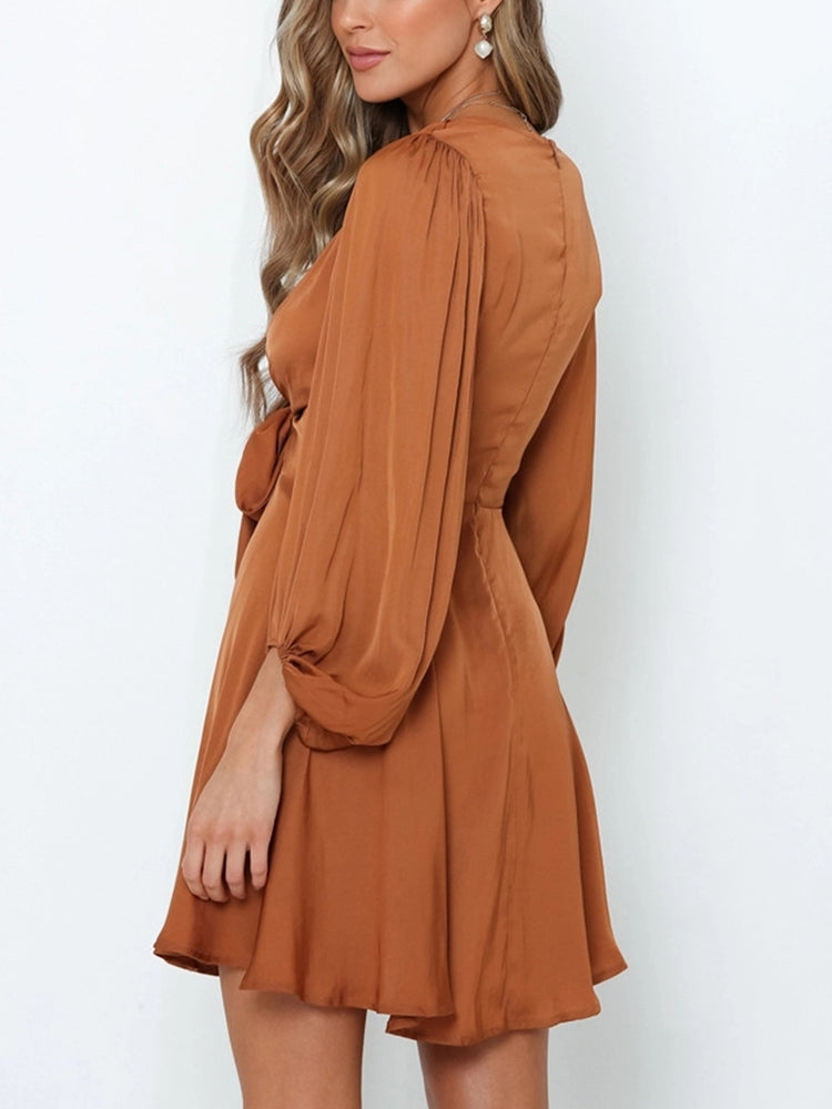back view of a woman wearing a brown satin mini dress with a tie-front detail and puffed sleeves