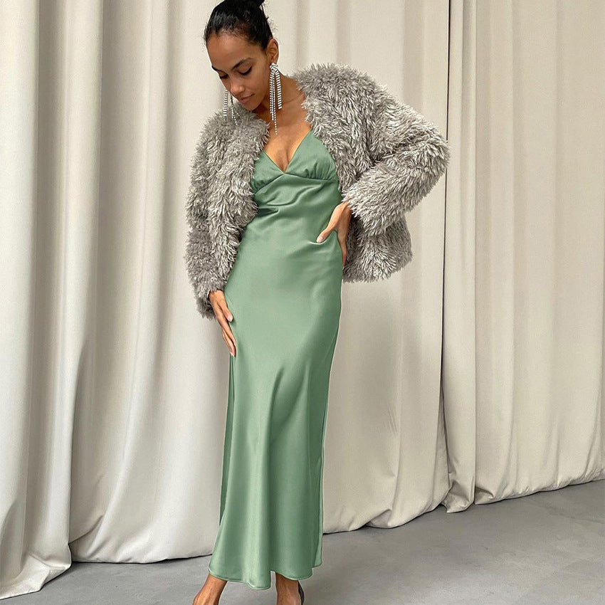 A woman models a green satin slip dress with a gray faux fur jacket, posing with hands on hips.