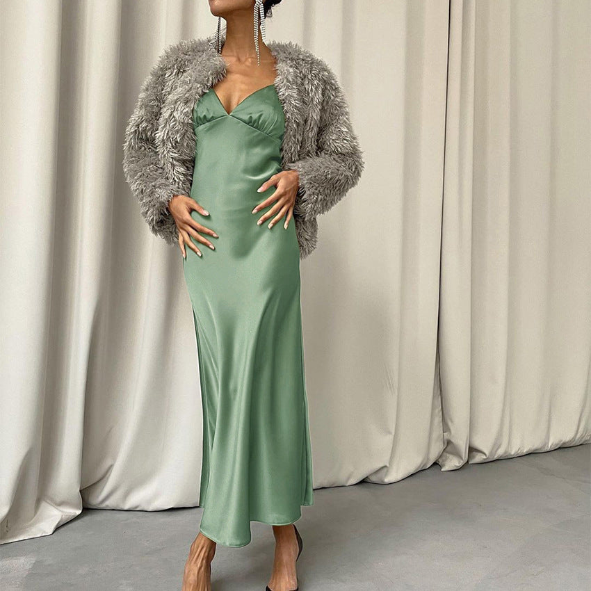 A woman models a green satin slip dress with a gray faux fur jacket.