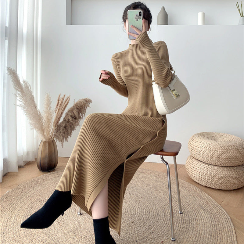 Woman wearing a long-sleeved, brown ribbed knit dress with a side slit, black socks, and black pointed-toe shoes, holding a white handbag.