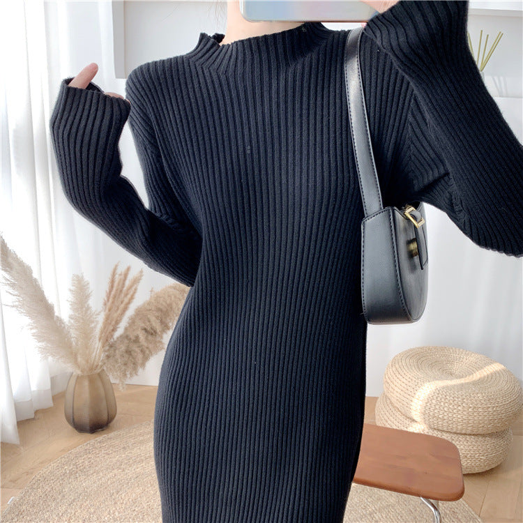 Close-up front view of a woman wearing a long-sleeved, black ribbed knit dress with a mock neck, holding a black handbag.
