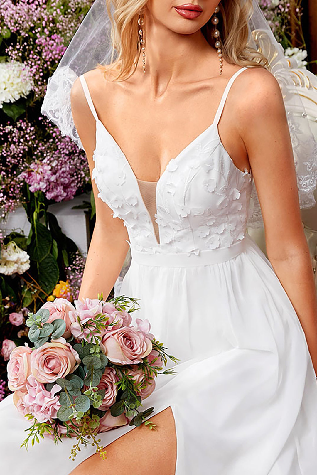 Close-up of the bodice of a white wedding dress with floral appliques and a plunging neckline, held by a woman holding a bouquet of pink roses.