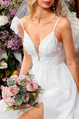Close-up of the bodice of a white wedding dress with floral appliques and a plunging neckline, held by a woman holding a bouquet of pink roses.