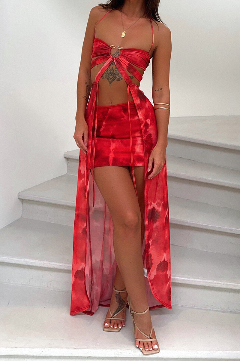 Full-body shot of a woman on stairs wearing a red tie-dye print dress with a halter top, mini skirt, and sheer maxi skirt overlay.