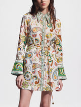 Woman wearing a white shirt dress with a colorful paisley print and bell sleeves.
