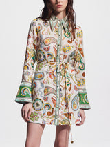 Front view of a woman wearing a white shirt dress with a colorful paisley print and bell sleeves.