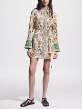 Woman wearing a white shirt dress with a colorful paisley print, bell sleeves, and black sandals.