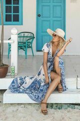 Woman in a blue and white floral maxi dress and a wide-brimmed hat sitting on a porch.
