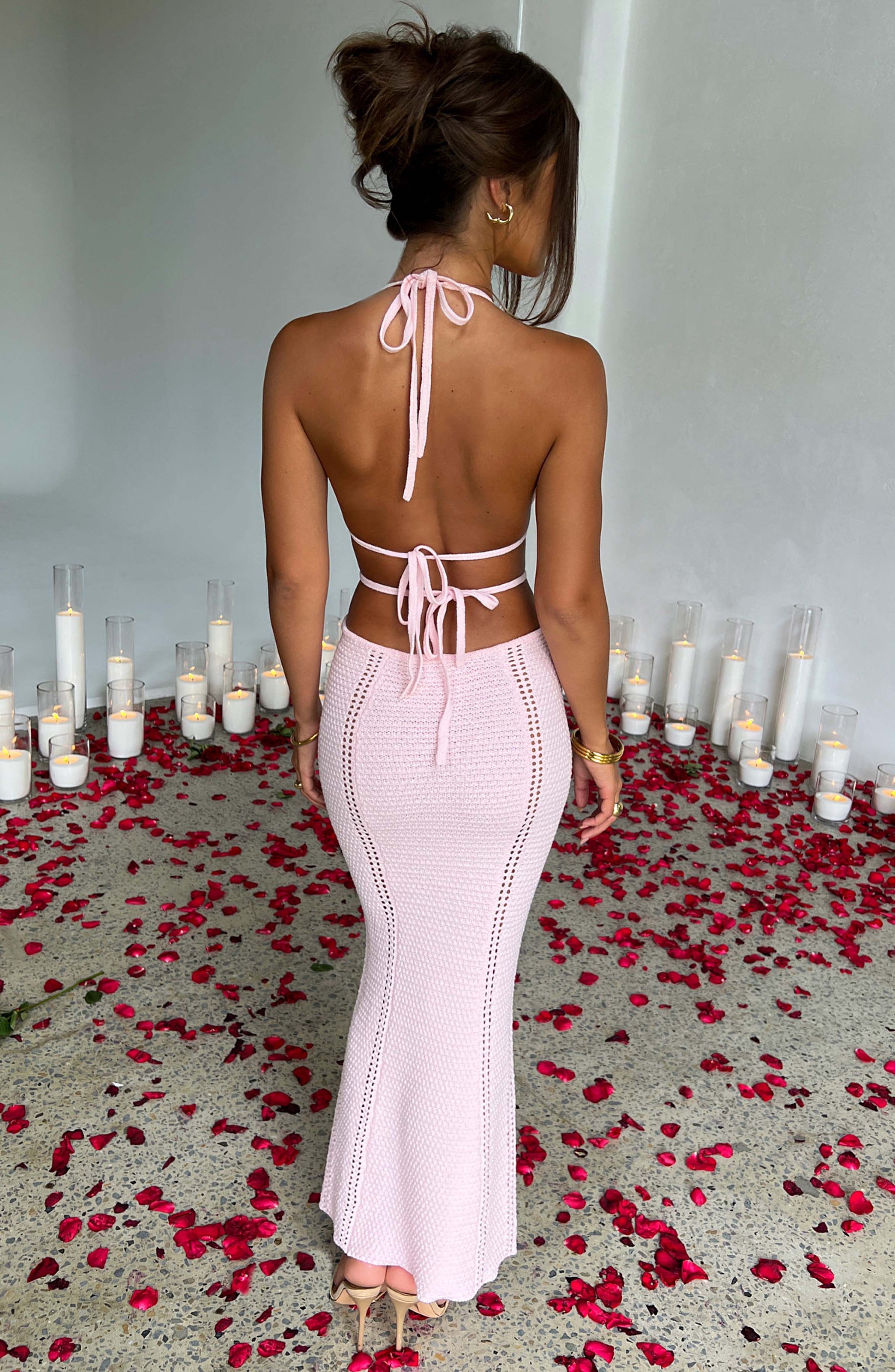 The back of a woman in a pink crocheted halter neck maxi dress with cut-outs, showing the tie-back closure.