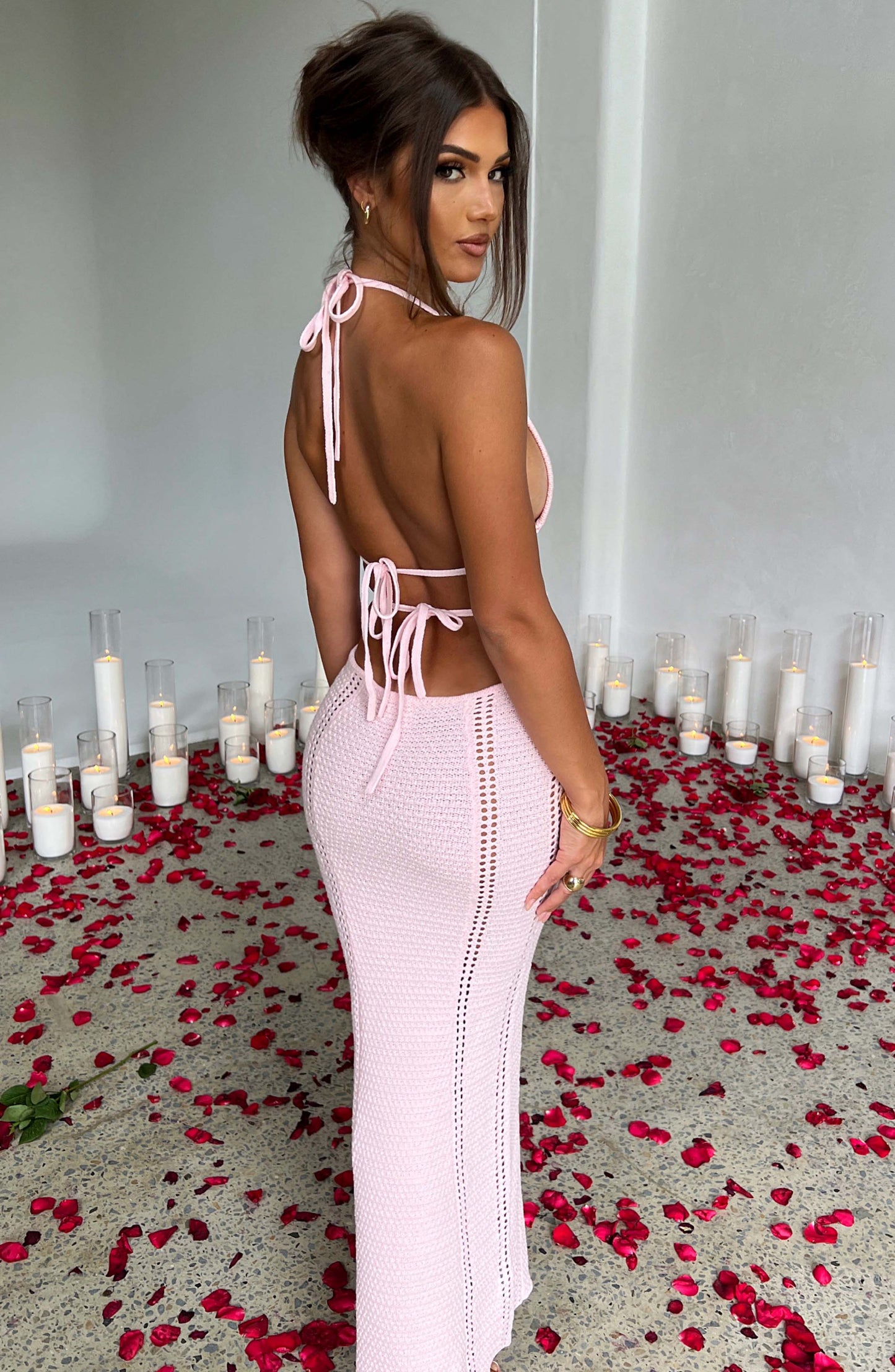 A side profile of a woman in a pink crocheted halter neck maxi dress, showcasing the cut-outs and silhouette.
