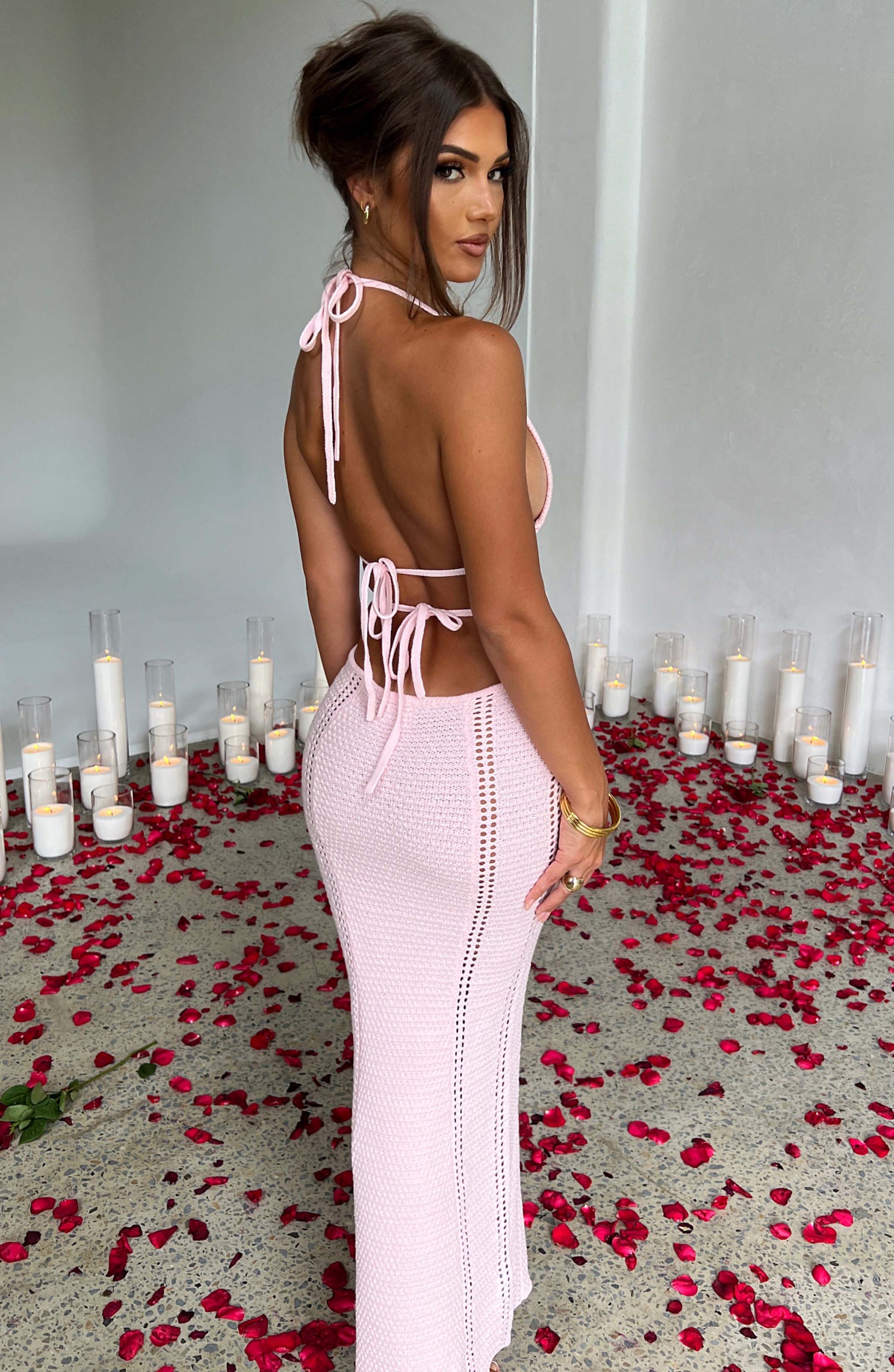 A side profile of a woman in a pink crocheted halter neck maxi dress, showcasing the cut-outs and silhouette.