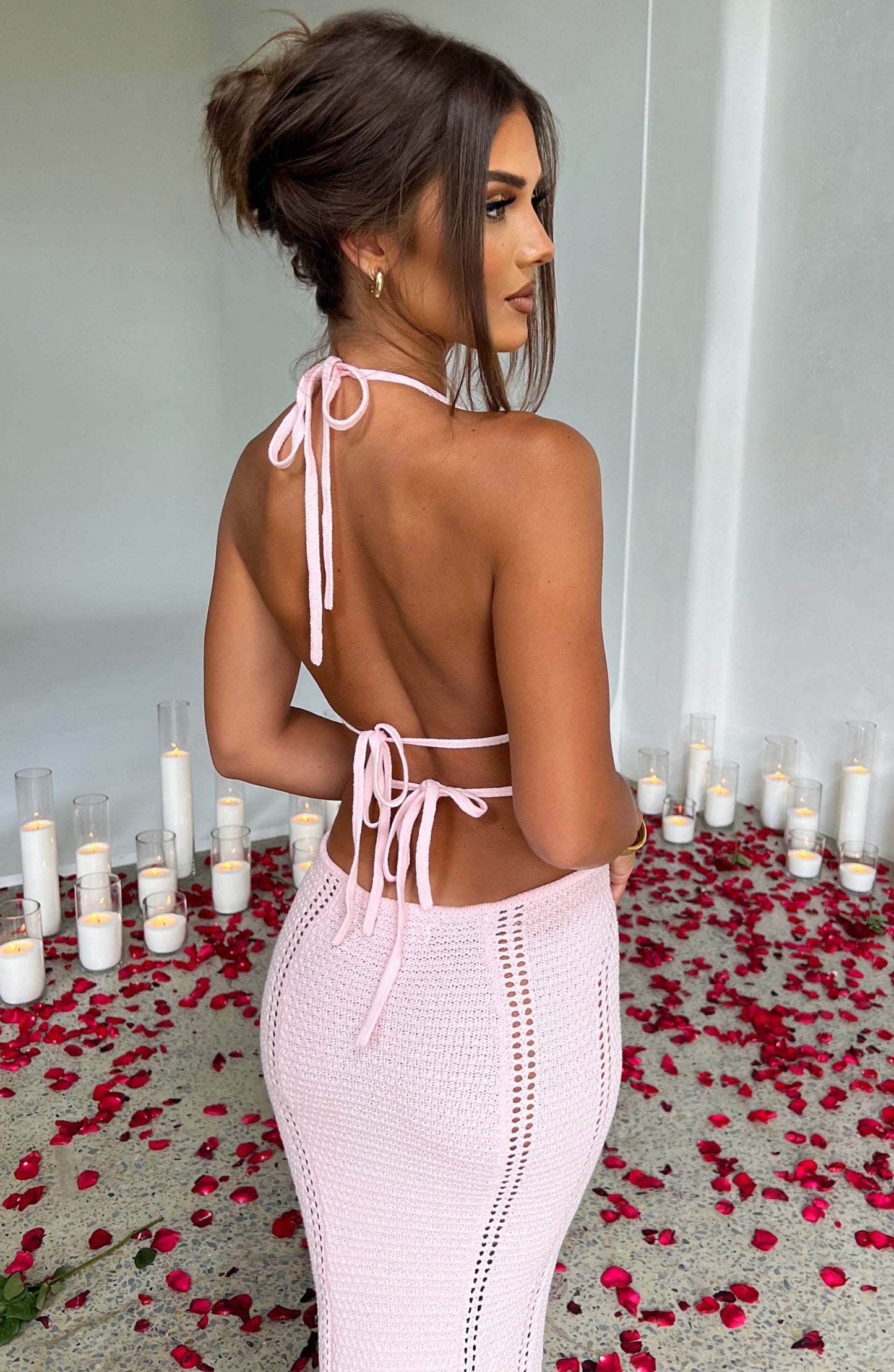 A rear view of a woman in a pink crocheted halter neck maxi dress, highlighting the open back and tie details.