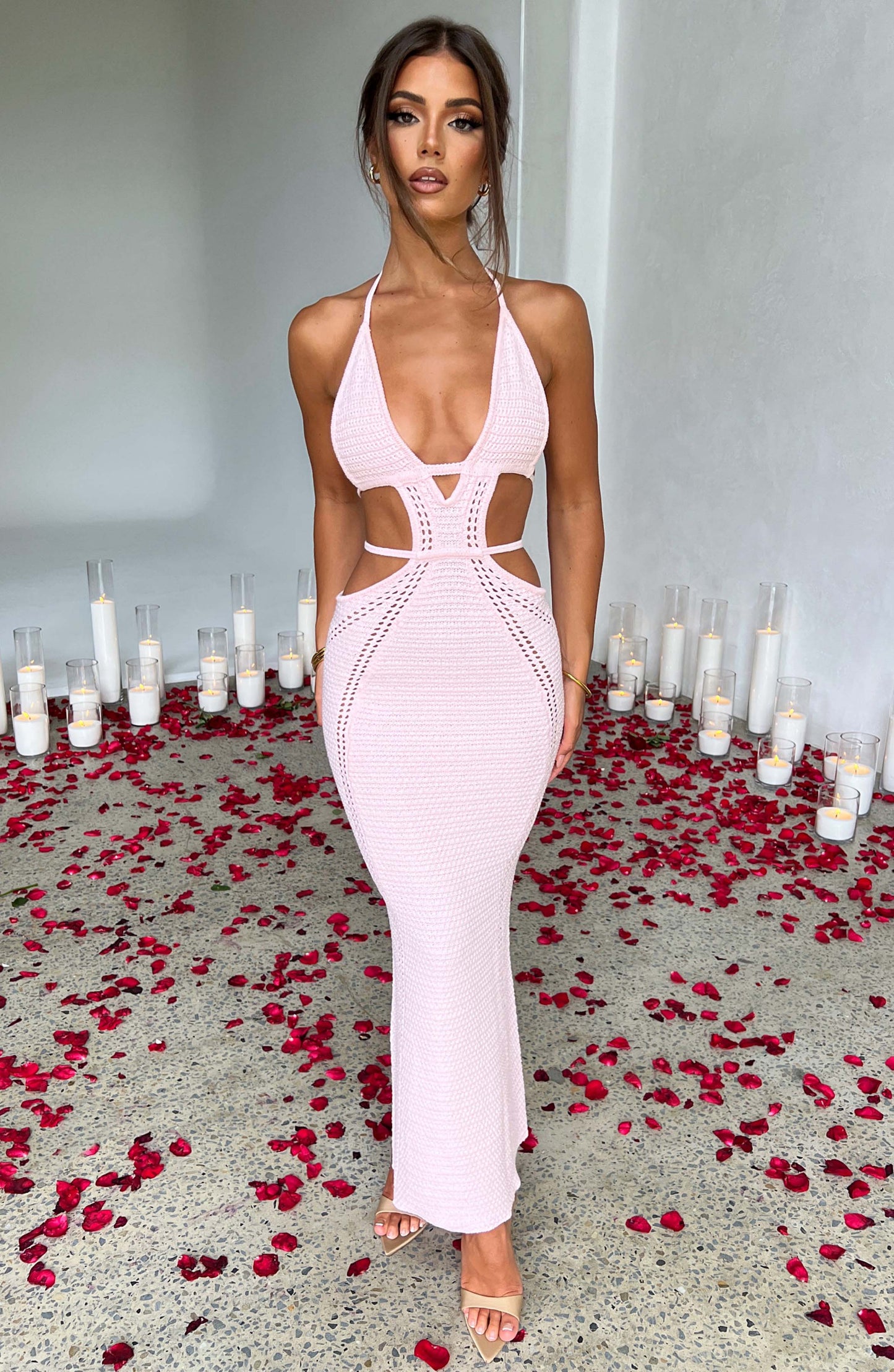 A full front view of a woman wearing a pink crocheted halter neck maxi dress with cut-outs.