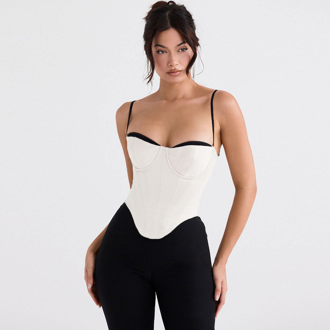 A woman wearing a white satin corset top with black trim and spaghetti straps, paired with black pants.