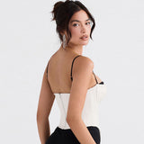 A woman wearing a white satin corset top with black trim and spaghetti straps, looking over her shoulder.