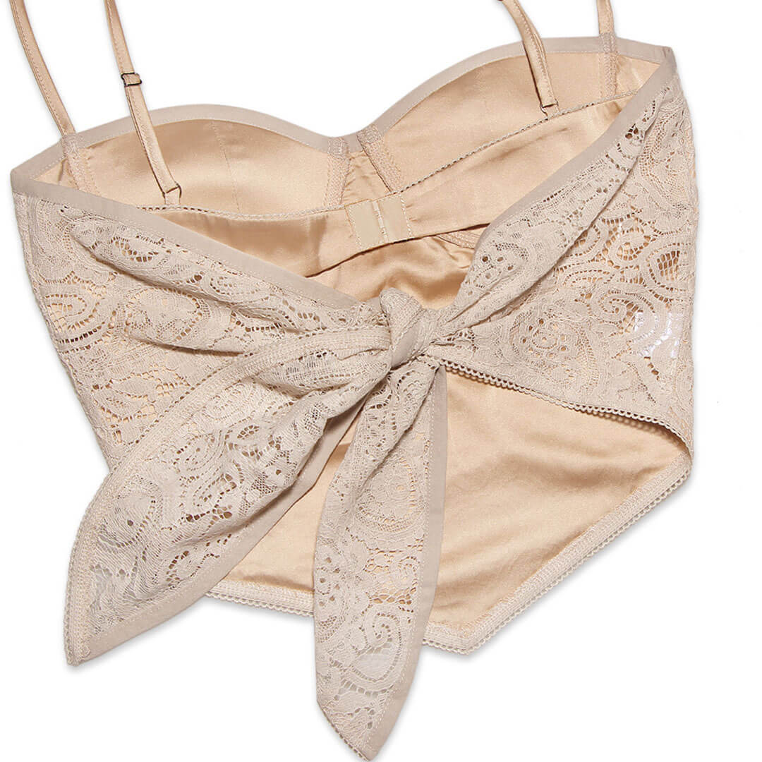 A beige lace corset top, shown from the back, with a satin lining and a lace bow tie closure