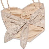 A beige lace corset top, shown from the back, with a satin lining and a lace bow tie closure