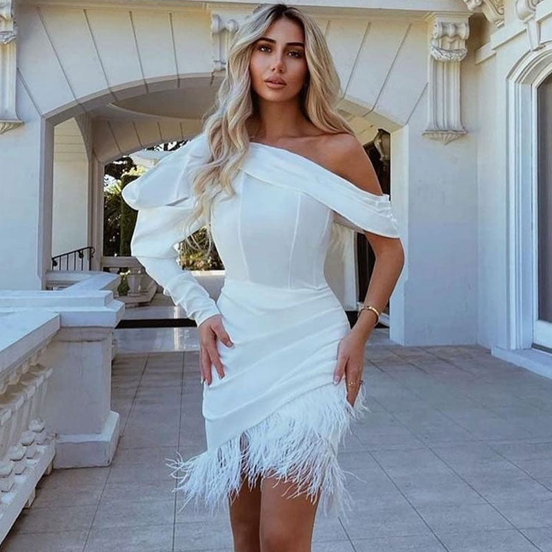 Woman in a white one-shoulder dress with feather trim standing outdoors