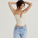 Woman wearing a cream strapless leather corset top and light wash jeans, with her hands in her hair.