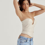 Close-up side view of a woman wearing a cream strapless leather corset top and light wash jeans, with her hands in her hair.