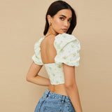 Back view of a woman wearing a white floral print corset top with puff sleeves.