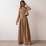 A woman in a brown cropped top and wide-leg pants stands with her hand on her head.