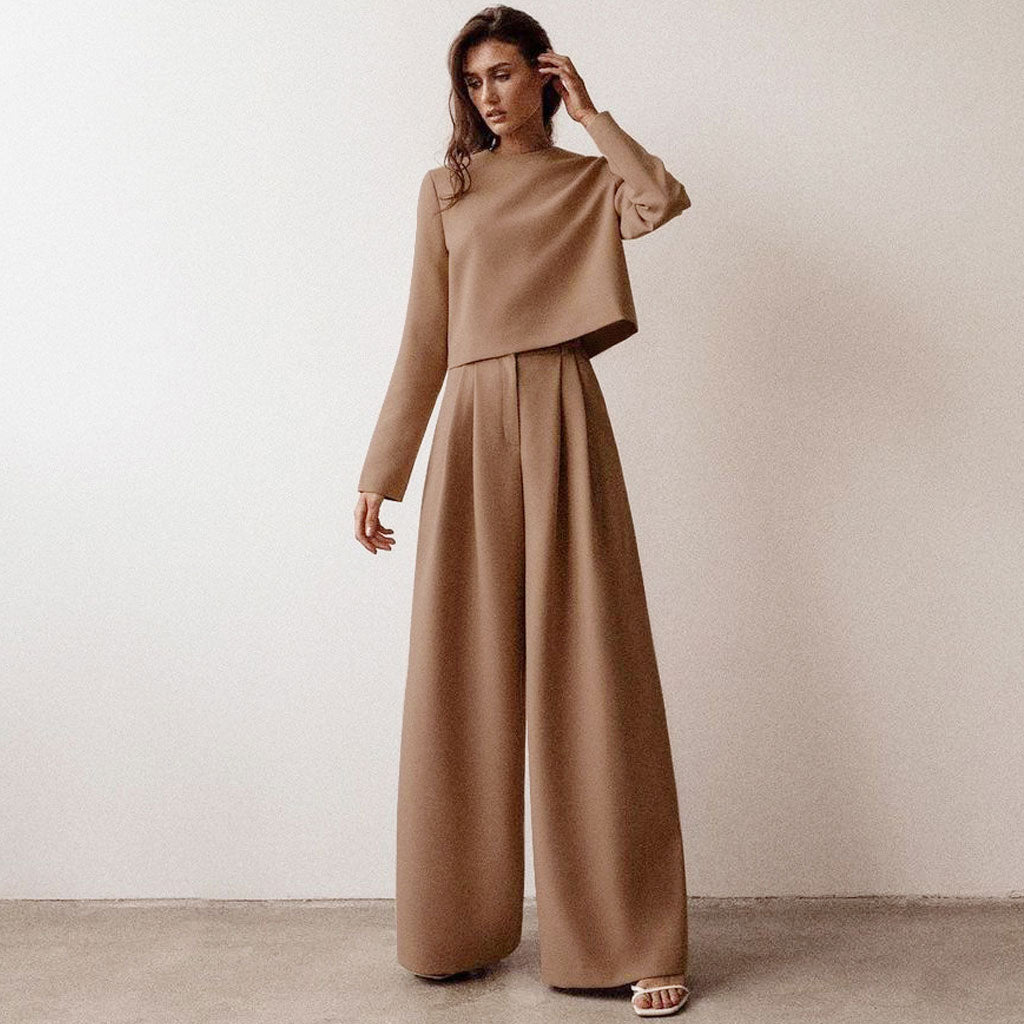 A woman in a brown cropped top and wide-leg pants stands with her hand on her head.