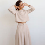 A woman with her eyes closed touches her face while wearing a beige outfit.