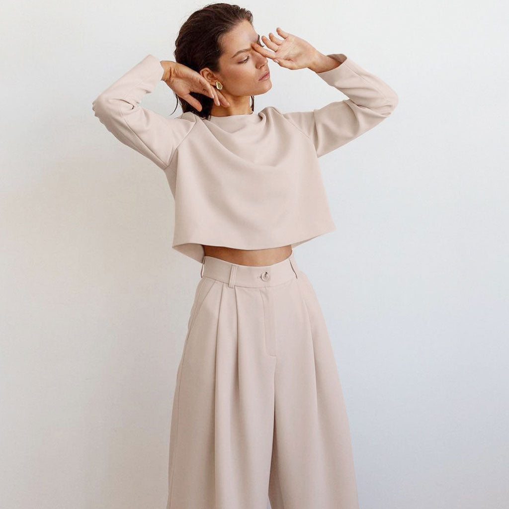 A woman with her eyes closed touches her face while wearing a beige outfit.