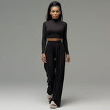 A woman wearing a black long-sleeved crop top and black wide-leg pants walks towards the camera.