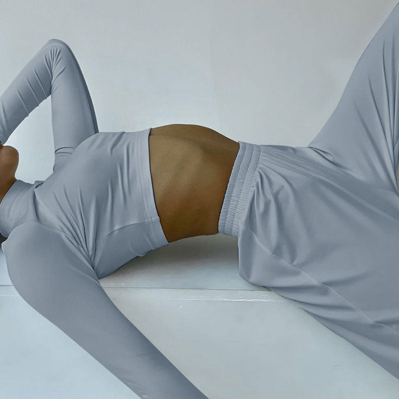 A woman in a gray crop top and wide-leg pants lies on her back.