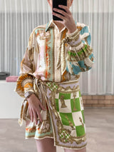 woman taking a mirror selfie wearing a white, green, orange, blue, pink, and yellow patterned silk shirt dress with a tie waist and puffed sleeves