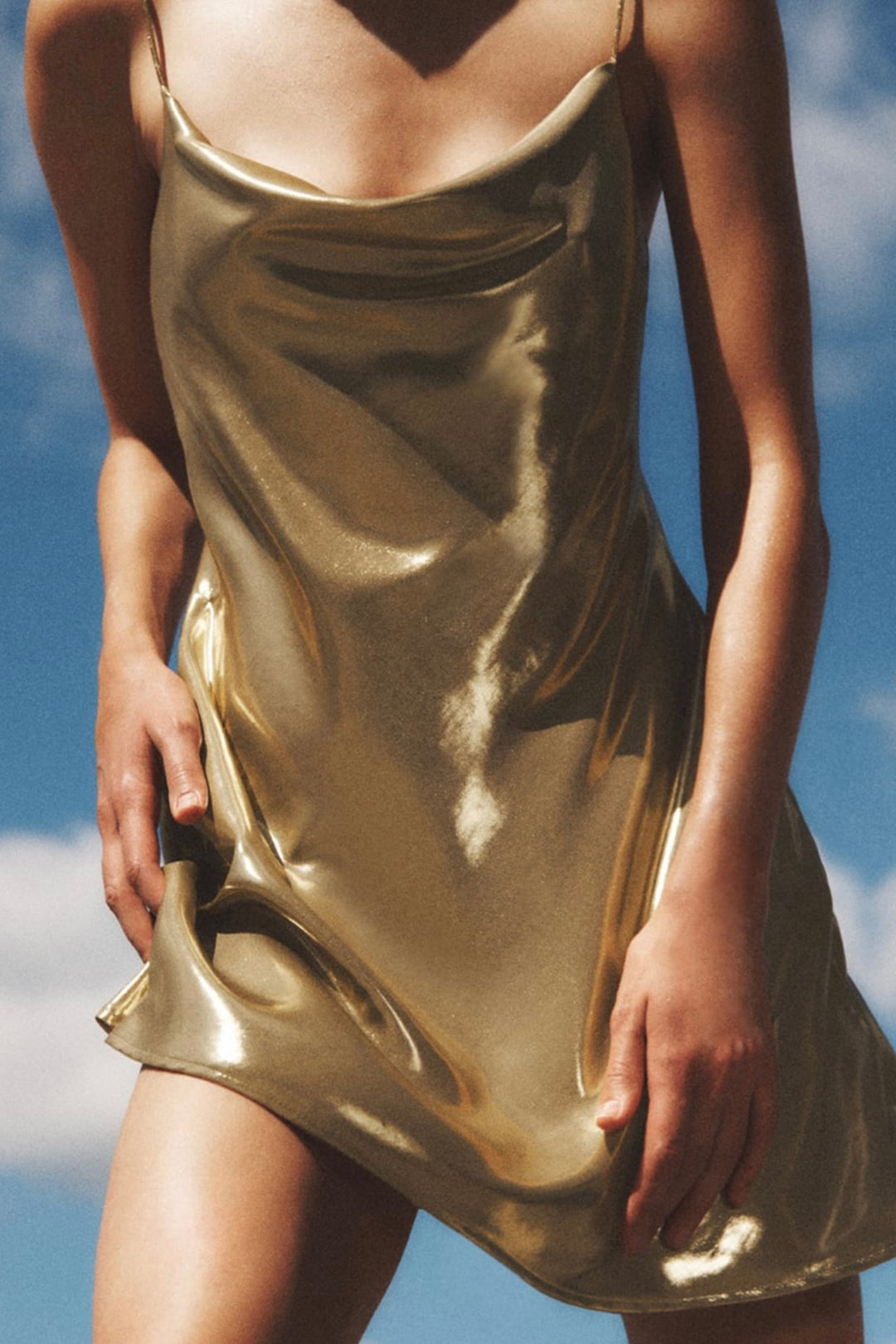 A woman wearing a gold slip dress outdoors with a blue sky in the background.