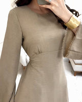 Close-up of a woman's upper body wearing a beige dress with bell sleeves, a gold cuff bracelet, and holding a brown handbag.