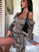 Woman in a leopard print off-the-shoulder dress with puff sleeves and a sweetheart neckline, sitting on a table.