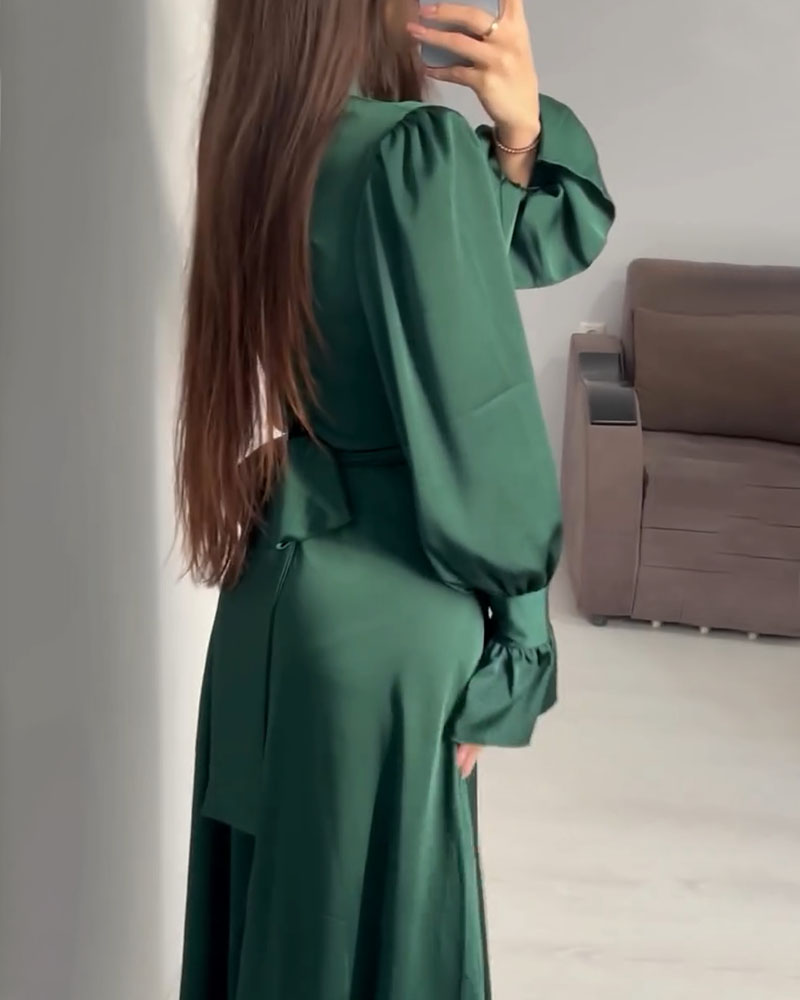 Rear view of a woman wearing a long emerald green satin dress, showing the back and the flow of the skirt.