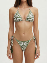 Front view of a woman wearing a white and green patterned bikini with a halter top and tie-side bottoms with tassels.