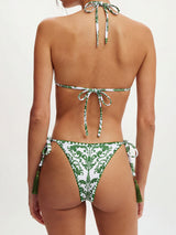 Back view of a woman wearing a white and green patterned bikini with a halter top and tie-side bottoms with tassels.