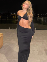 A woman in a black one-shoulder, cut-out maxi dress with a twist-front detail stands on a balcony at night.