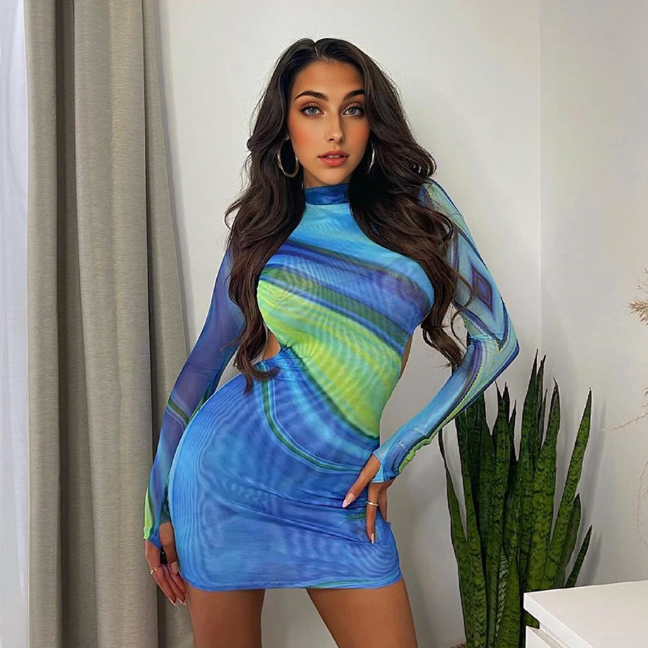 Woman in a blue and green abstract print mesh mini dress with cut-out sides, standing indoors