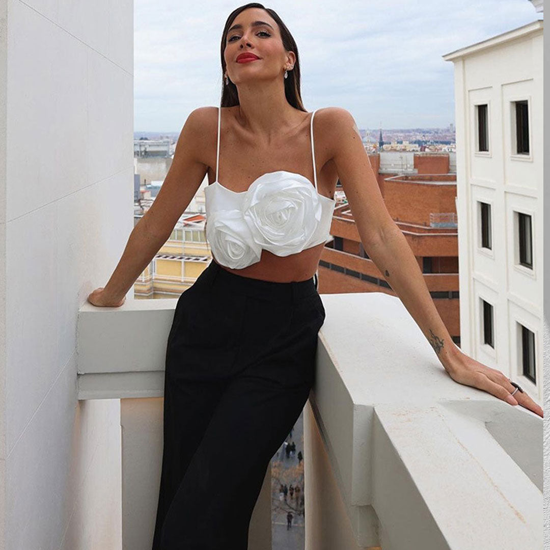 Woman leaning on a balcony railing wearing a white floral crop top and black pants