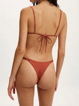 Back view of a woman wearing a rust-colored bikini with string ties at the back of the top and bottom.