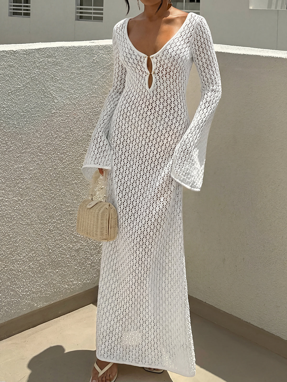 Woman wearing a white crochet knit maxi dress with bell sleeves and a deep V-neck.